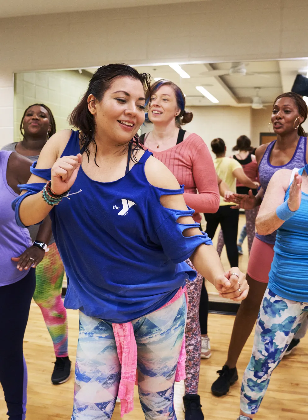 A group of diverse people in athletic attire dance joyfully in a fitness class, holding hands, and smiling broadly.
