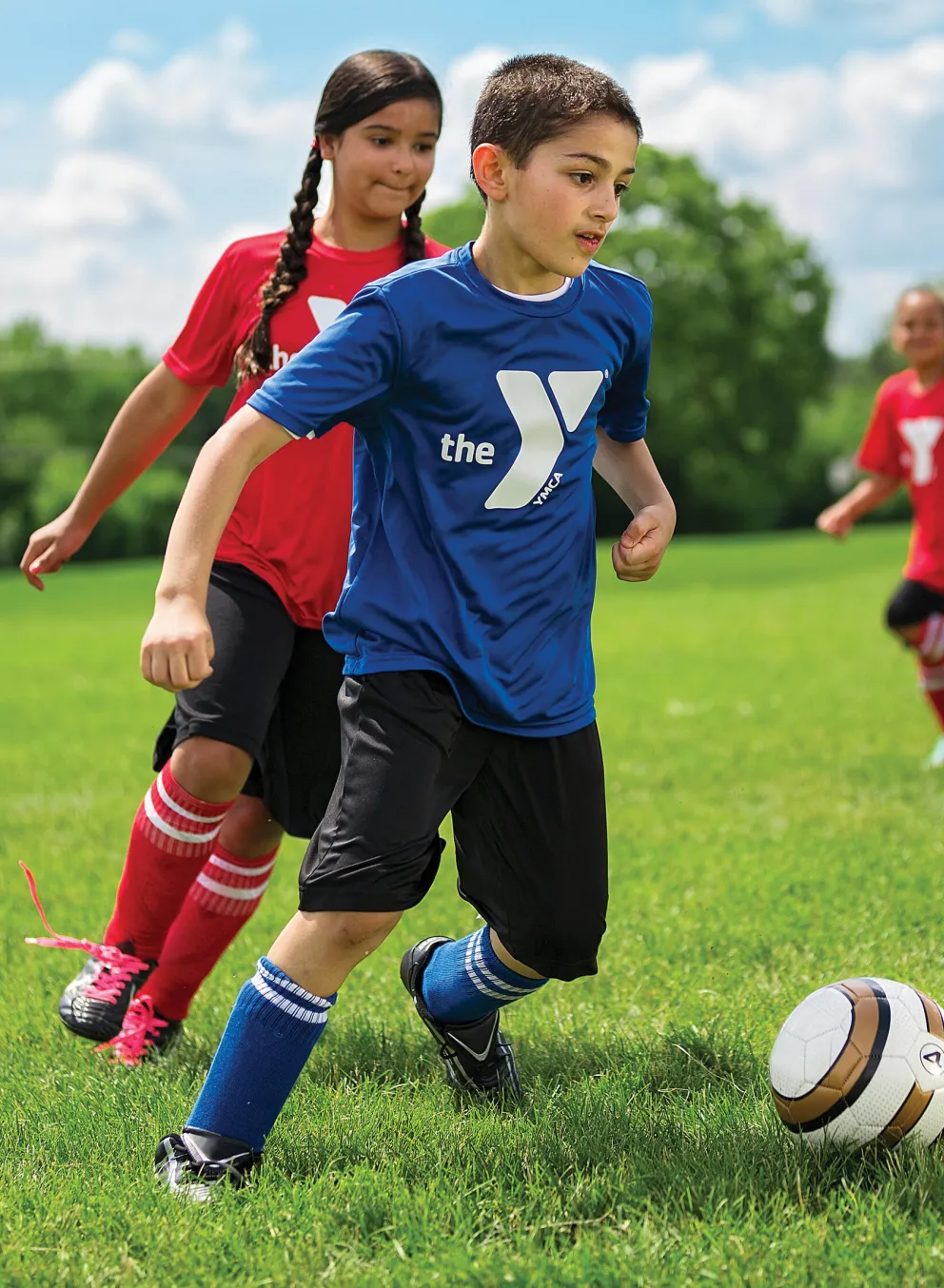 Children playing soccer on a green field; a coach observes. A boy in blue runs toward the ball while other children are playing.